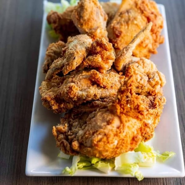 Crispy fried chicken pieces with lettuce garnish on a white rectangular plate.