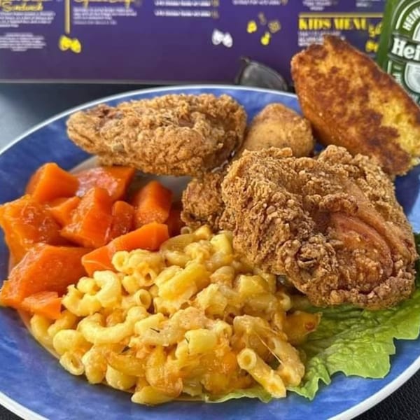 A soul food plate with fried chicken, macaroni and cheese, candied yams, and cornbread.