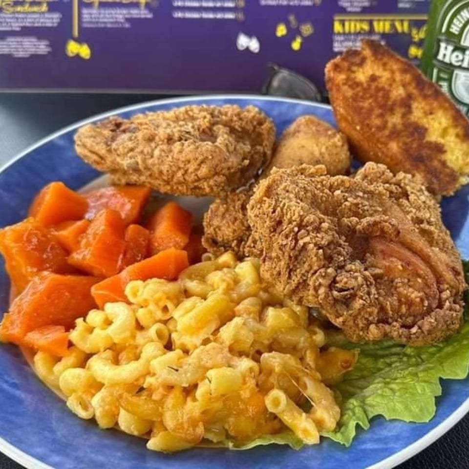 A soul food plate with fried chicken, macaroni and cheese, candied yams, and cornbread.