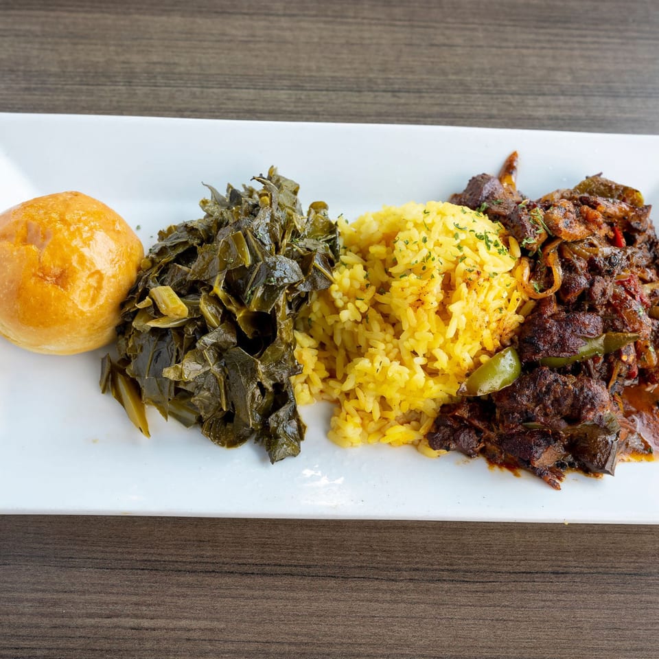 A soul food plate with a golden roll, collard greens, yellow rice, and stewed meat.