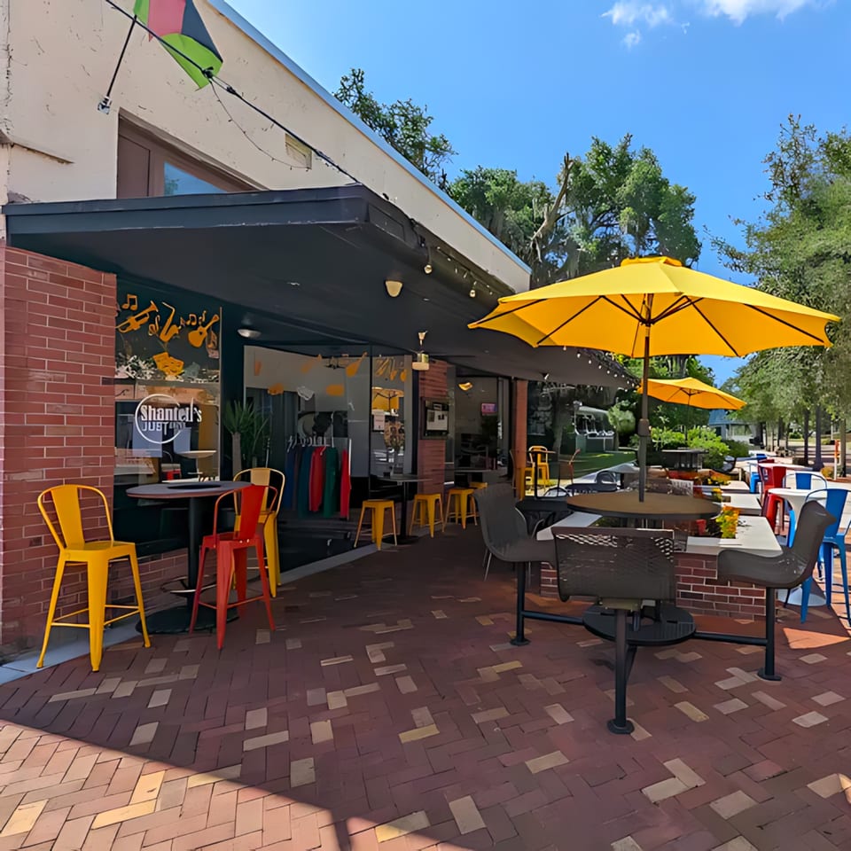 Shantell's Just Until Restaurant & Lounge's outdoor patio with yellow umbrellas, colorful chairs, and brick flooring.