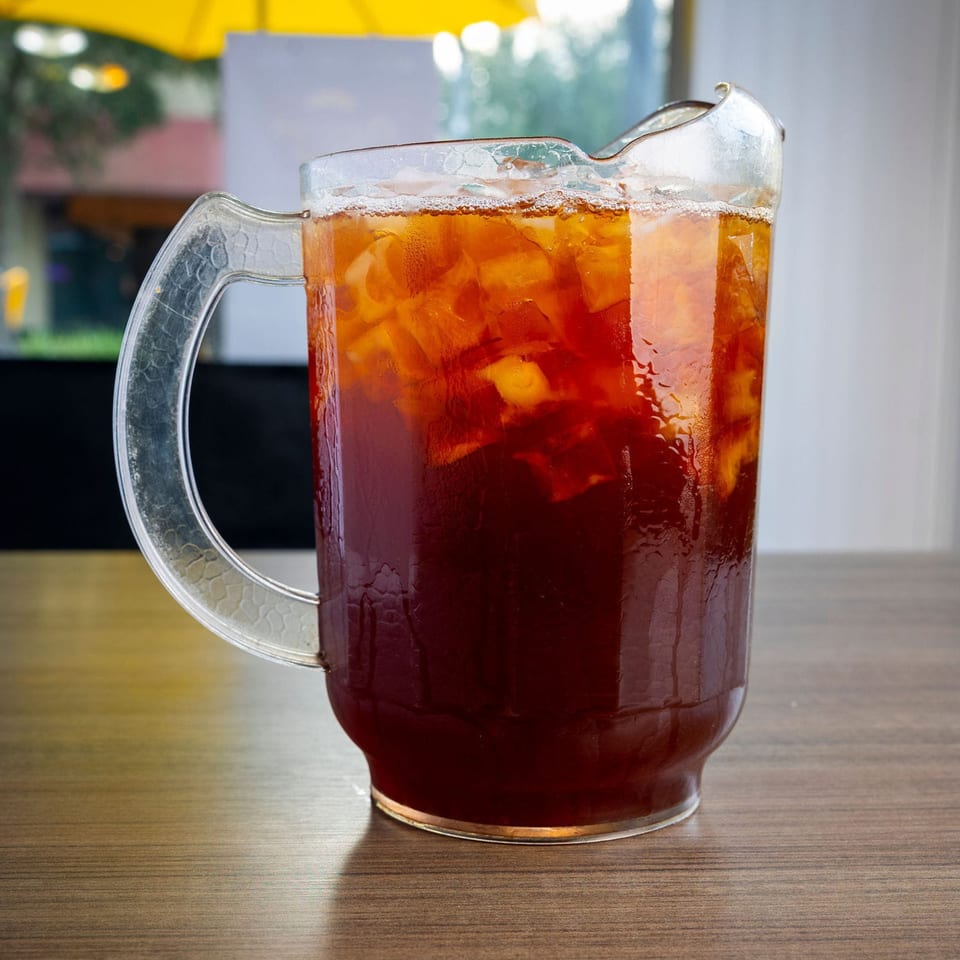 A clear pitcher of iced tea with ice cubes sits on a wooden table at Shantell's.