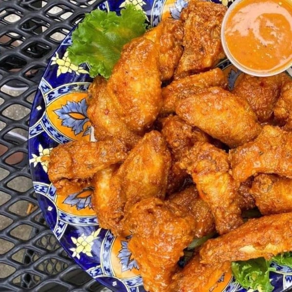 A plate of crispy fried chicken wings with a side of dipping sauce and lettuce.