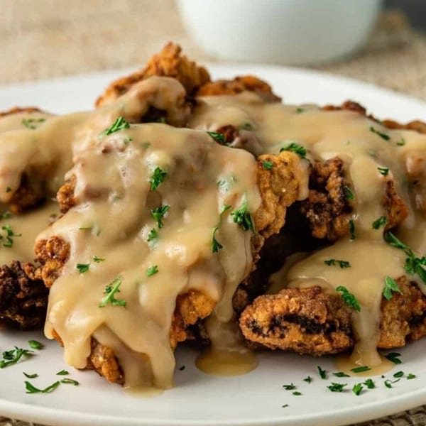 Crispy fried chicken pieces covered in creamy gravy and garnished with fresh parsley on a white plate.