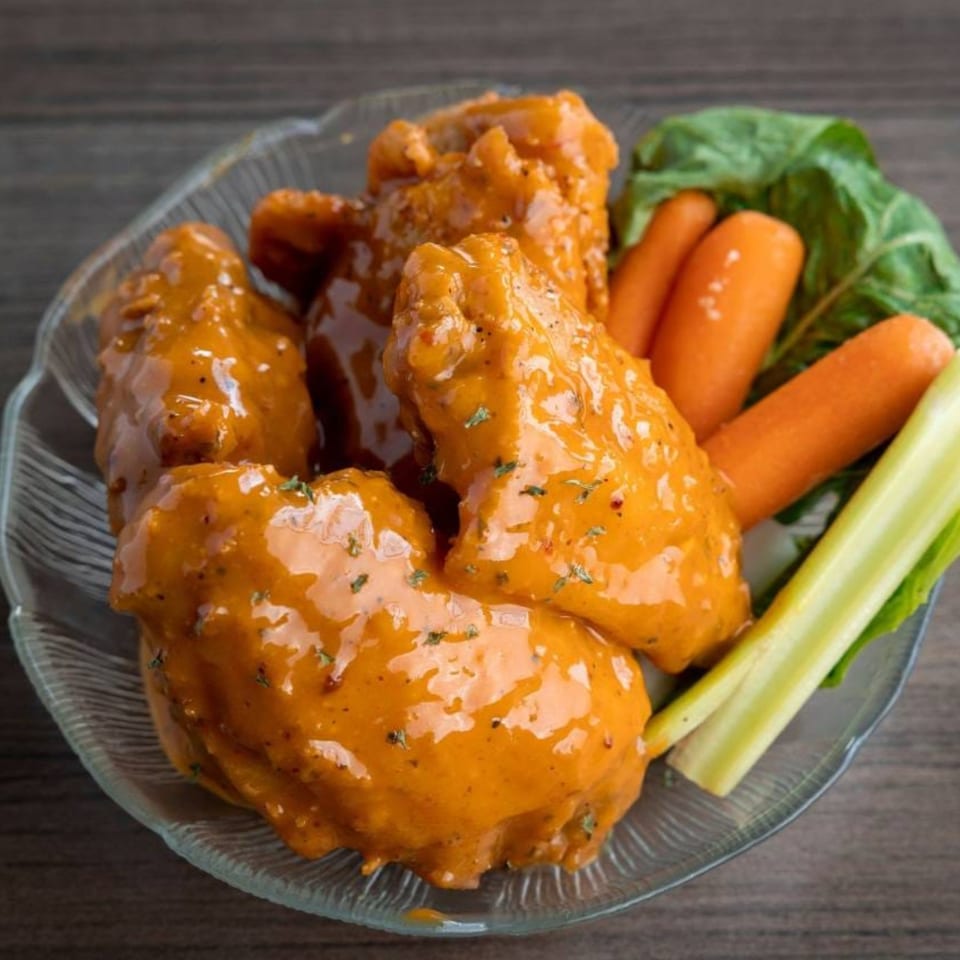 A bowl of Shantell's Just Until Restaurant & Lounge's buffalo wings with carrots and celery.
