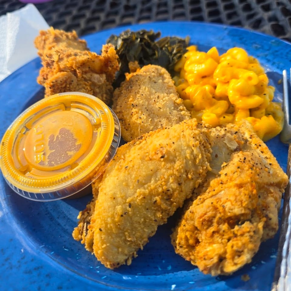 A soul food plate with fried chicken, macaroni and cheese, collard greens, and dipping sauce.