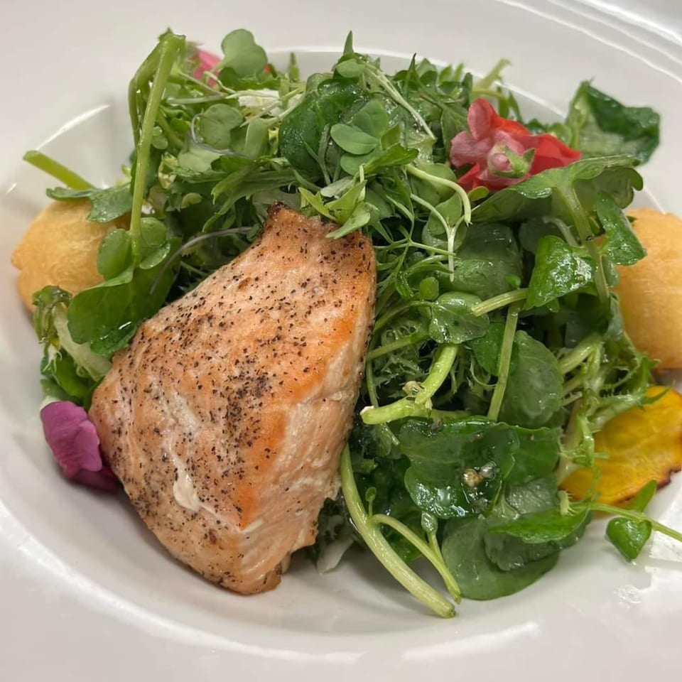 A perfectly cooked salmon fillet rests on a bed of fresh green salad with edible flowers and yellow accents.
