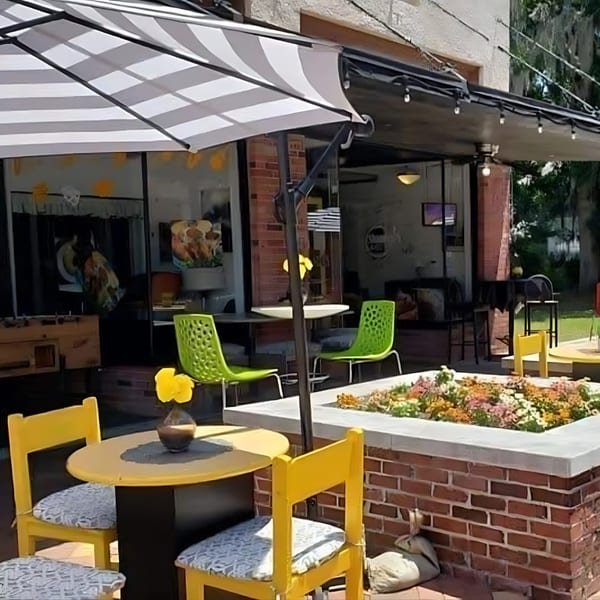 Outdoor patio at Shantell's Just Until Restaurant & Lounge with yellow and green seating, and a striped umbrella.