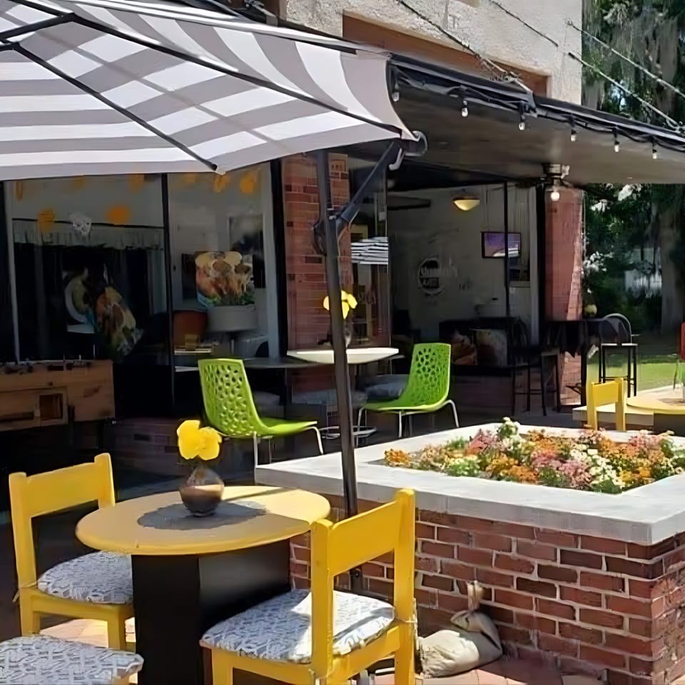 Outdoor patio at Shantell's Just Until Restaurant & Lounge with yellow and green seating, and a striped umbrella.