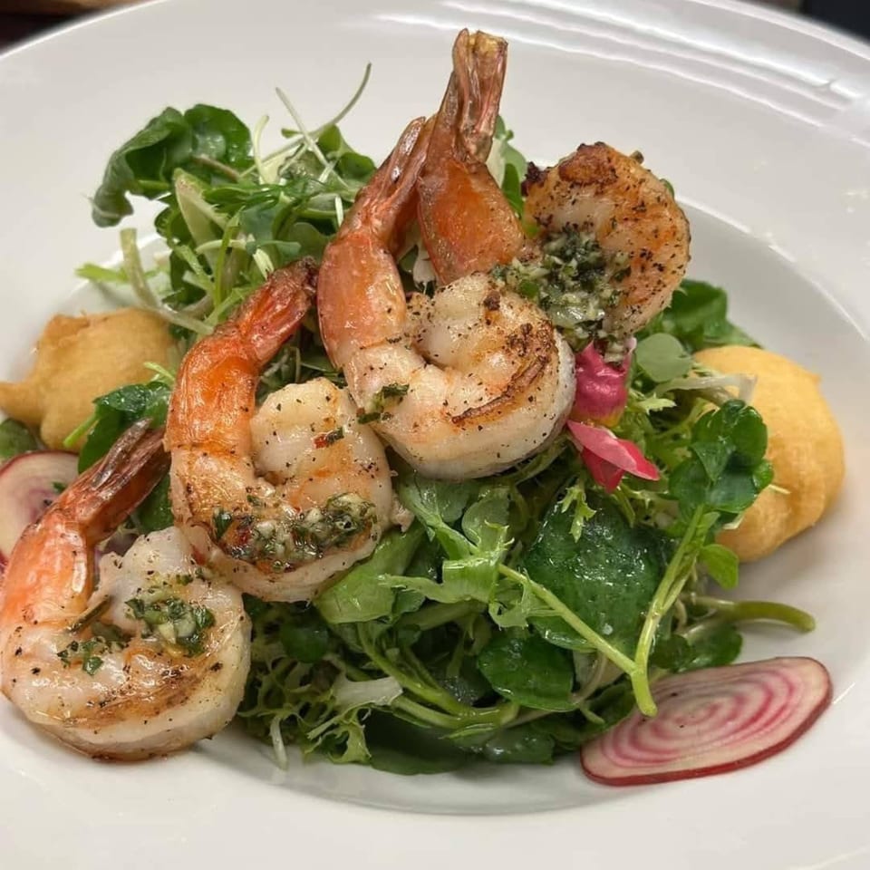 Grilled shrimp on a bed of fresh greens with sliced radishes and hush puppies.