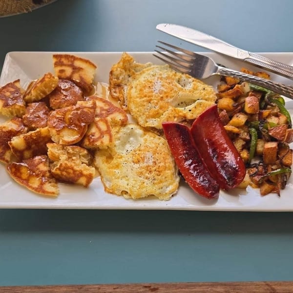 A soul food breakfast plate with mini pancakes, eggs, sausage, and home fries with peppers.