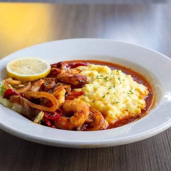 Soul food shrimp and grits with a lemon slice, bell peppers, and onions in a white bowl.